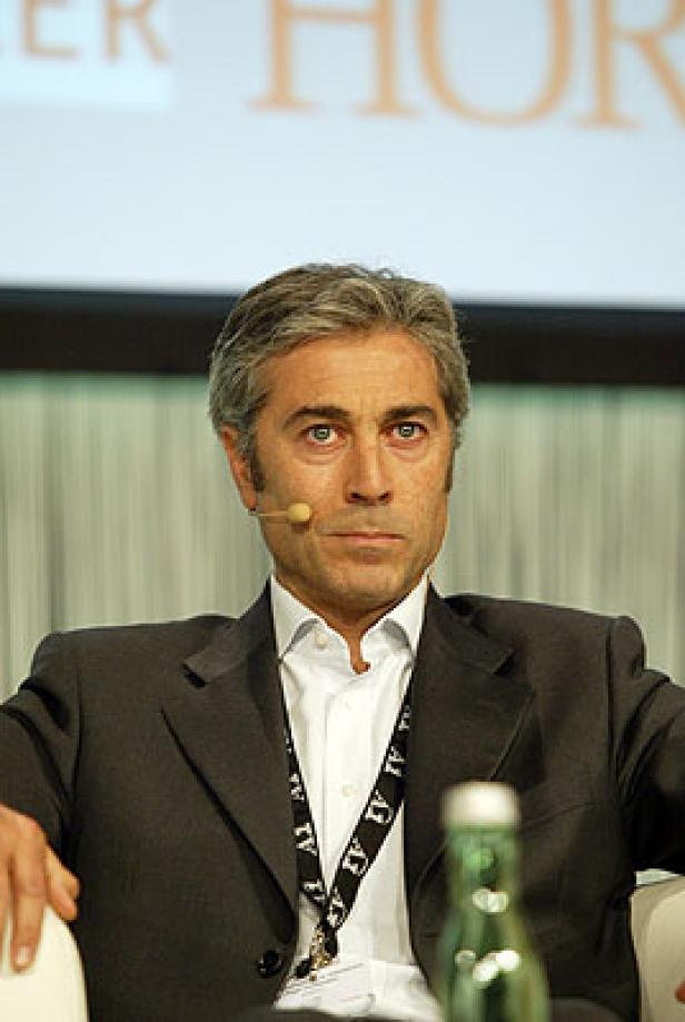 Ein Mann mit grau meliertem Haar und Anzug sitzt bei einer Konferenz.