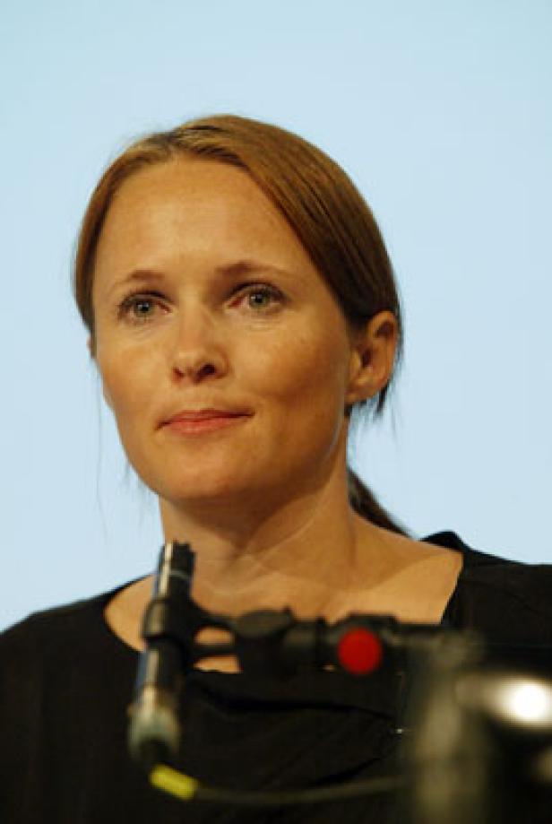 Eine Frau mit rötlich-braunen Haaren steht vor einem Mikrofon.