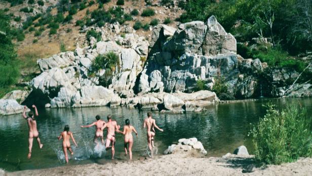 Eine Gruppe unbekleideter Menschen rennt in einen Fluss.