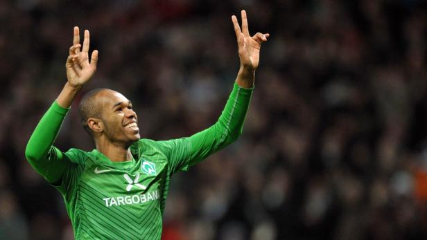 Ein Fußballspieler im grünen Trikot jubelt mit erhobenen Händen.