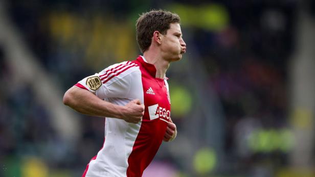 Ein Fußballspieler im rot-weißen Trikot des AFC Ajax läuft mit aufgeblähten Wangen.