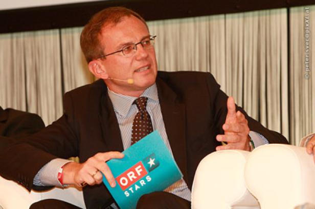 Ein Mann mit Brille und Anzug hält eine Broschüre mit der Aufschrift „ORF Stars“.