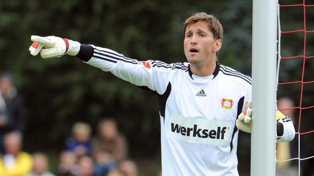 Ein Torwart in weißem Trikot mit Werkself-Aufdruck zeigt mit dem Finger nach links.