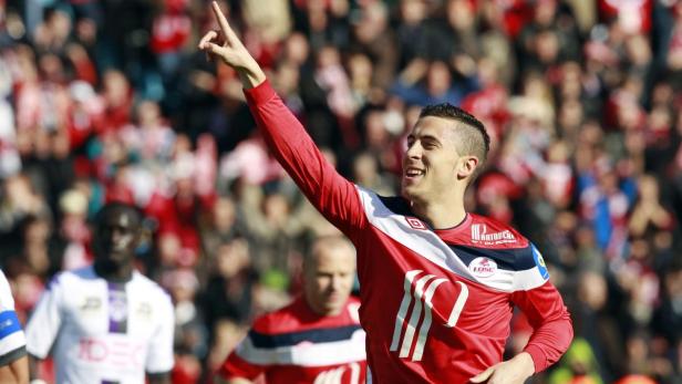 Ein Fußballspieler in rotem Trikot jubelt mit erhobenem Zeigefinger vor einer Zuschauermenge.