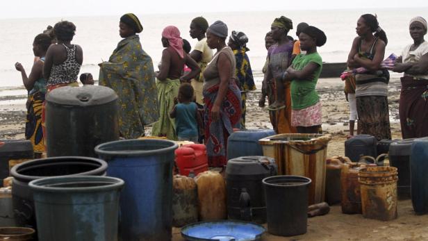 Eine Gruppe afrikanischer Frauen steht am Strand hinter vielen Eimern und Kanistern.
