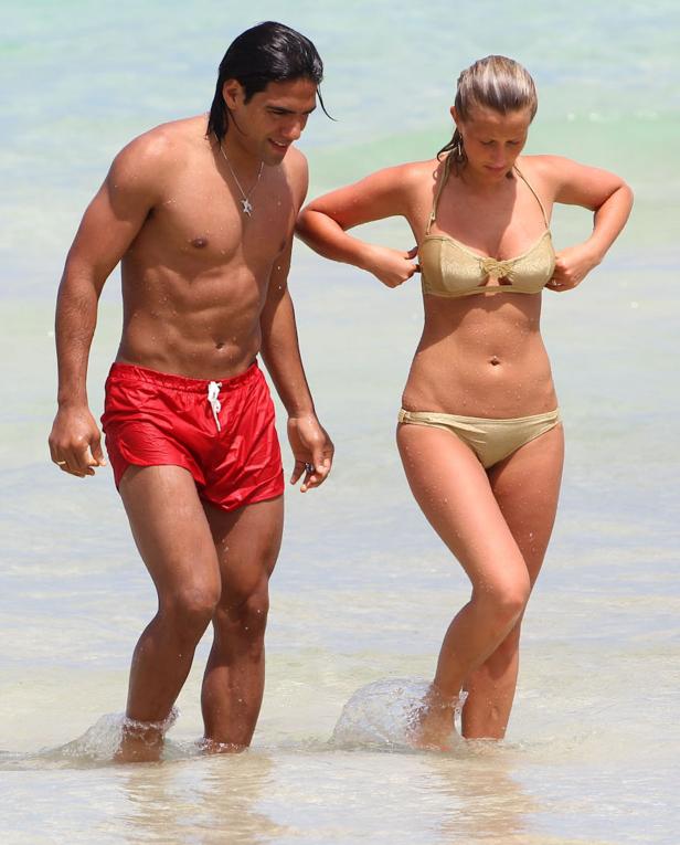 Ein Mann in roter Badehose und eine Frau im goldenen Bikini stehen im flachen Wasser.