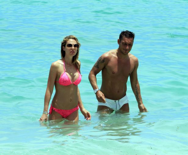 Ein Paar watet im türkisfarbenen Wasser eines Strandes.