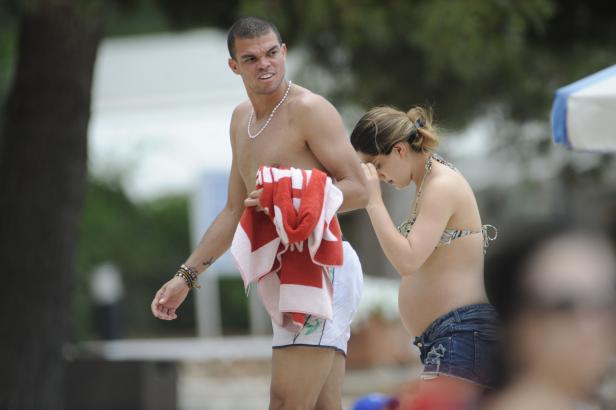 Ein Mann mit Badehose und Handtuch steht neben einer schwangeren Frau am Strand.