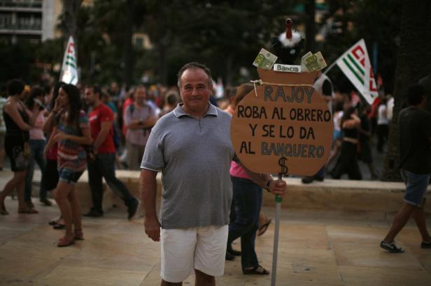 Ein Mann demonstriert mit einem Schild, das „Rajoy raubt dem Arbeiter und gibt es dem Bankier“ zeigt.