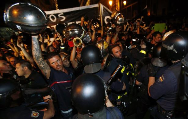 Feuerwehrleute demonstrieren mit erhobenen Helmen gegen Polizisten.
