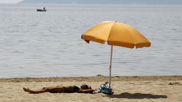 Eine Frau liegt am Strand unter einem gelben Sonnenschirm.