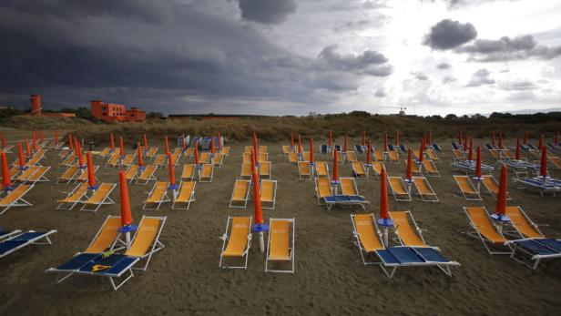 Viele leere Liegestühle und Sonnenschirme stehen an einem Strand unter einem dunklen Himmel.