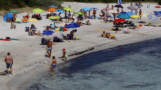 Ein Strand ist mit bunten Sonnenschirmen und vielen Menschen gefüllt.