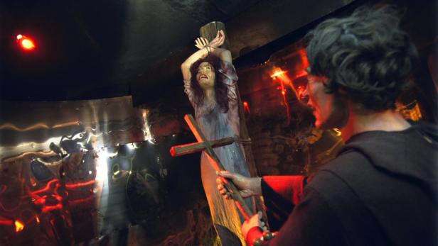 Eine gefolterte Frau ist an ein Holzkreuz gefesselt, während ein Mann ein Kreuz in der Hand hält.