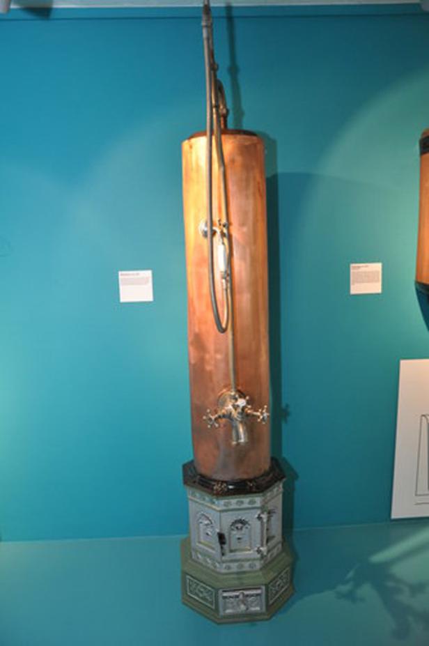 Eine alte Dusche aus Kupfer steht auf einem verzierten Sockel.