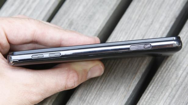Die Seite eines schwarzen Smartphones wird von einer Hand gehalten.