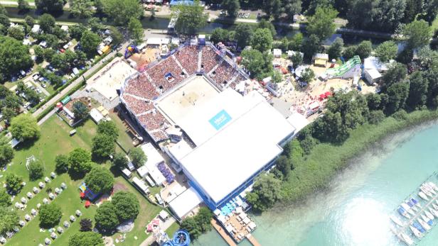 Luftaufnahme eines Beachvolleyballturniers mit Zuschauern am Ufer eines Sees.