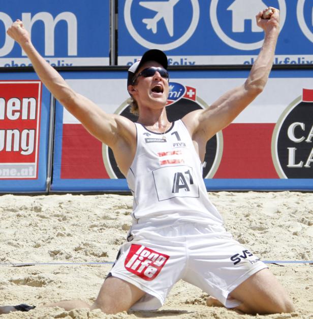 Ein Beachvolleyballspieler jubelt mit erhobenen Armen im Sand.