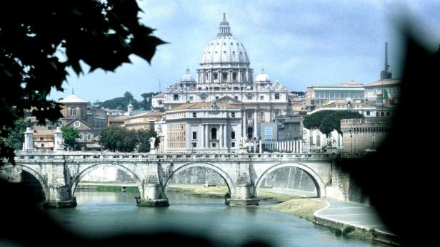 Blick auf den Petersdom in Rom über den Tiber und eine Brücke.