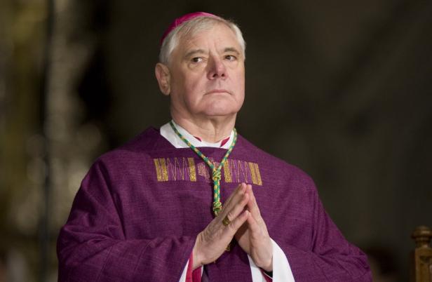 Ein Bischof in lila Gewändern mit gefalteten Händen.