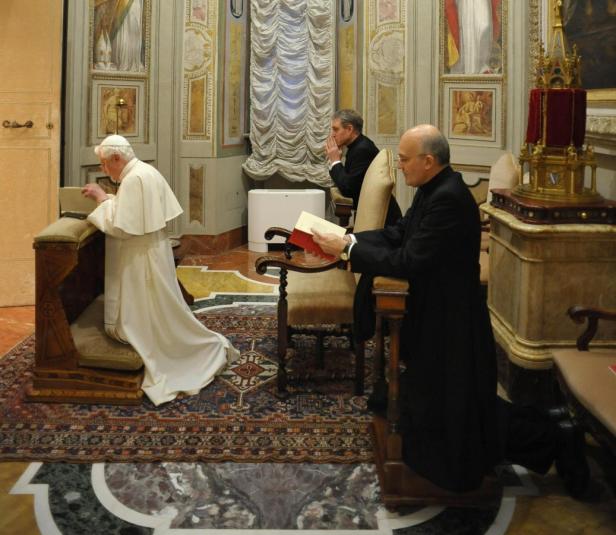 Papst Benedikt XVI. und zwei weitere Männer knien in einem reich verzierten Raum und beten.