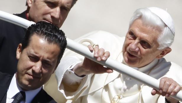 Papst Benedikt XVI. hält sich an einer Stange fest, während er von zwei Männern begleitet wird.