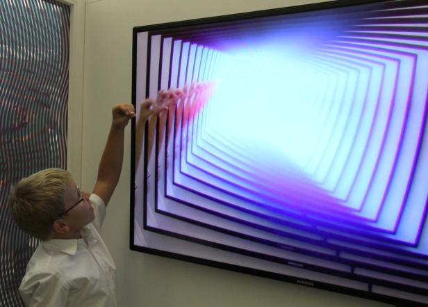 Ein Junge mit Brille interagiert mit einem interaktiven Display, das einen Tunnel darstellt.