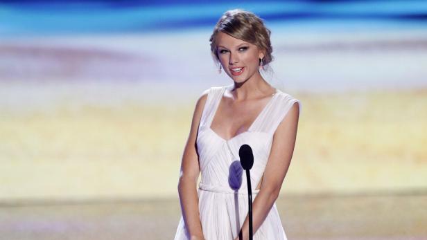 Taylor Swift in einem weißen Kleid steht an einem Mikrofon.