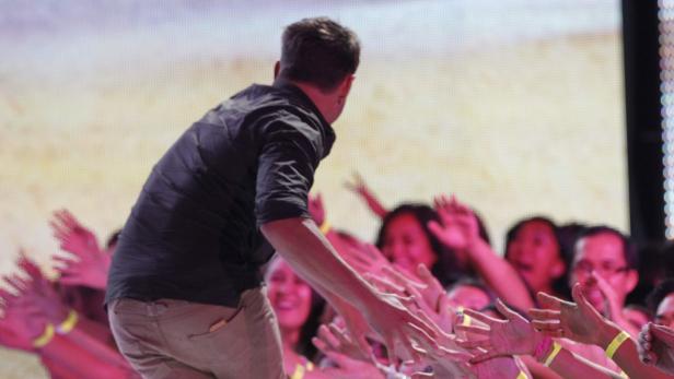 Ein Mann in Hemd und Hose reicht einer Menge die Hände.