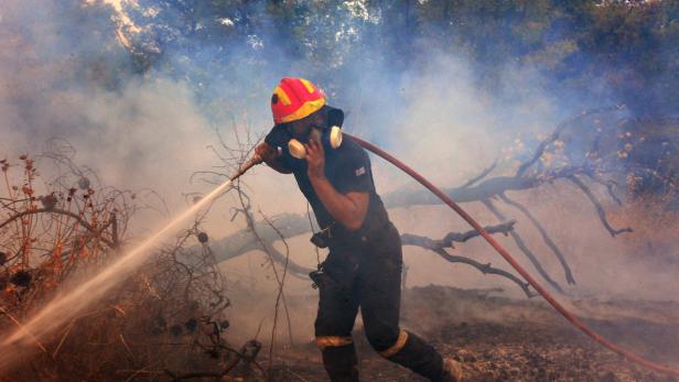Ein Feuerwehrmann bekämpft mit einem Schlauch einen Waldbrand.