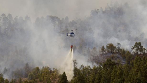 Ein Hubschrauber löscht mit einem Wasserbehälter einen Waldbrand.