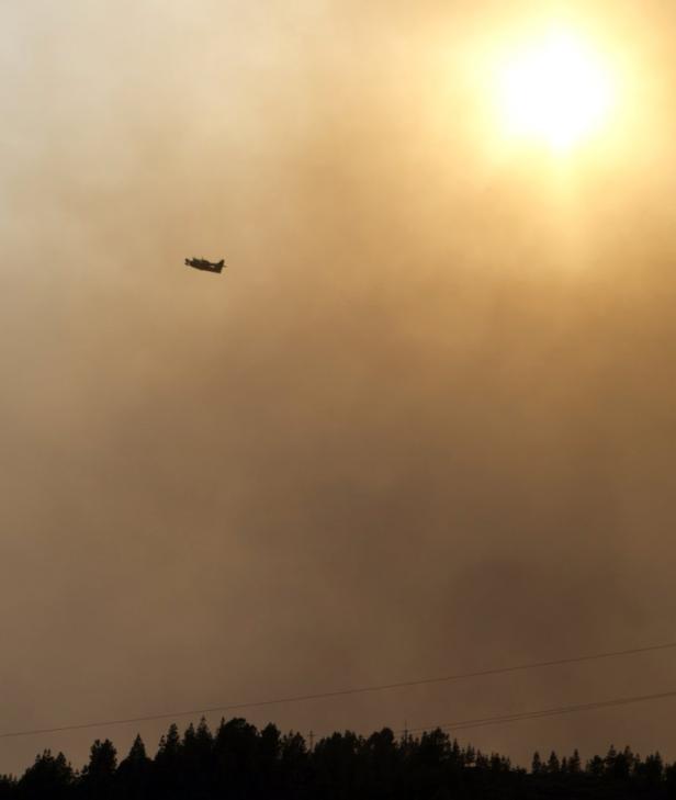 Ein Löschflugzeug fliegt vor einem orangefarbenen, rauchverhangenen Himmel.