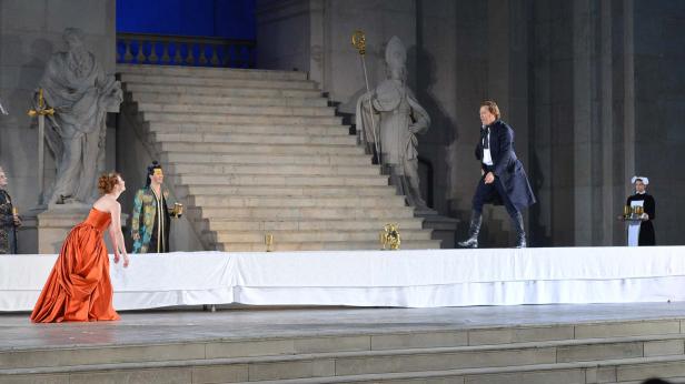 Eine Theaterszene mit Schauspielern vor einer monumentalen Treppe und Statuen.