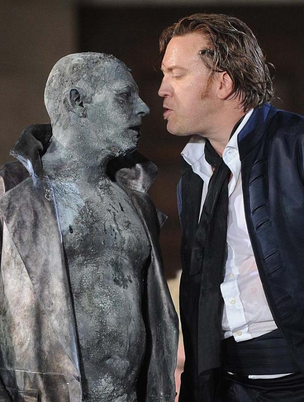 Ein Mann im Anzug scheint mit einer Statue zu sprechen.