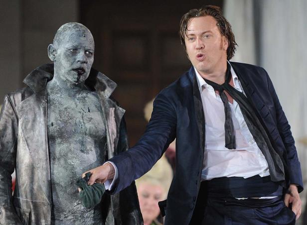 Ein Mann im Anzug interagiert mit einer Figur, die wie eine Statue aussieht.