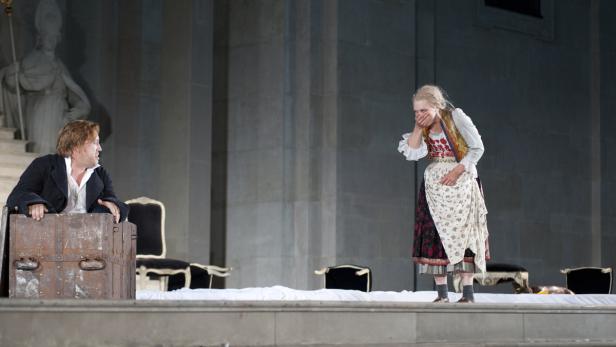 Eine Szene aus einem Theaterstück mit einem Mann in einer Kiste und einer erschrockenen Frau.