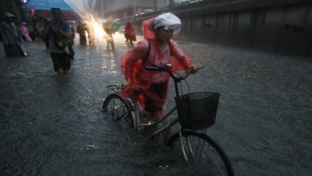 Eine Frau schiebt ihr Fahrrad durch eine überschwemmte Straße im Regen.
