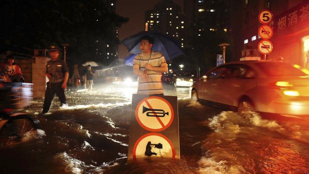 Ein Mann steht im Hochwasser mit einem Schild, das Hupen verbietet.