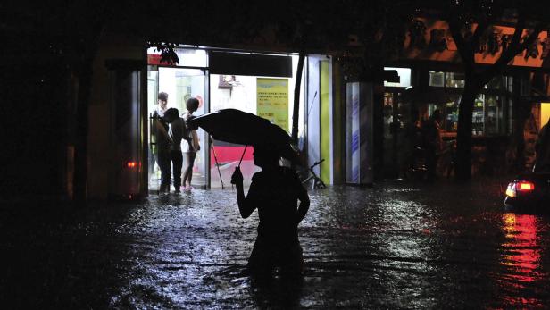 Eine Person mit Regenschirm watet durch das Hochwasser in einer dunklen Straße.