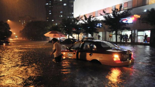 Ein Mann watet durch eine überflutete Straße neben einem Taxi im Regen.
