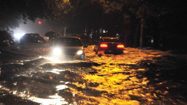 Autos fahren nachts durch eine überflutete Straße.