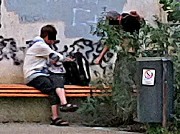 Ein Jugendlicher sitzt auf einer Bank vor einer Wand mit Graffiti.