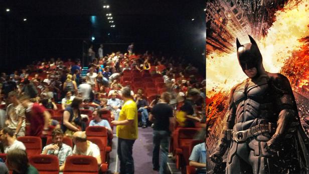 Ein Kinosaal voller Menschen vor einem Poster von „The Dark Knight Rises“.