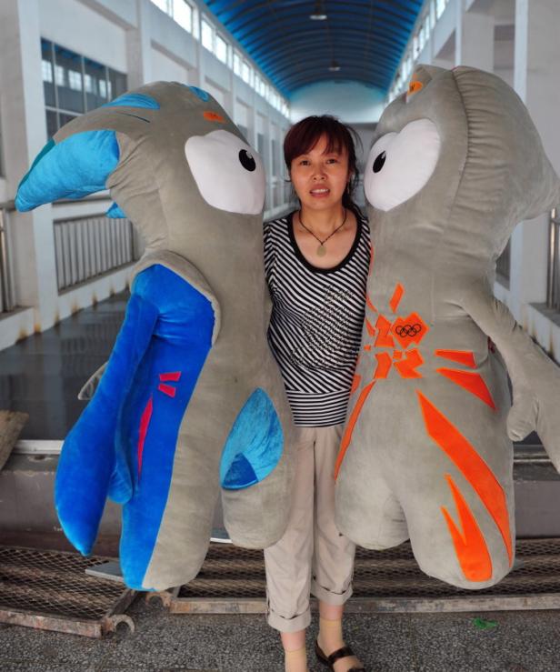 Eine Frau steht zwischen zwei Maskottchen mit dem Logo der Olympischen Spiele.
