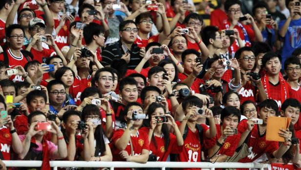 Eine große Menschenmenge, viele davon in roten Manchester United Trikots, fotografiert mit ihren Handys und Kameras.
