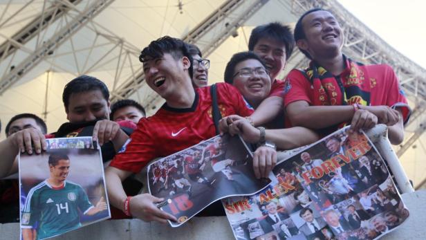 Eine Gruppe asiatischer Fußballfans hält Poster von Fußballspielern und -trainern hoch.