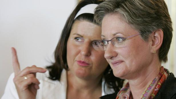 Zwei Frauen stehen nebeneinander, eine mit erhobenem Zeigefinger.