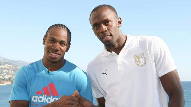 Usain Bolt posiert mit einem anderen Mann vor einem Küstenhintergrund.