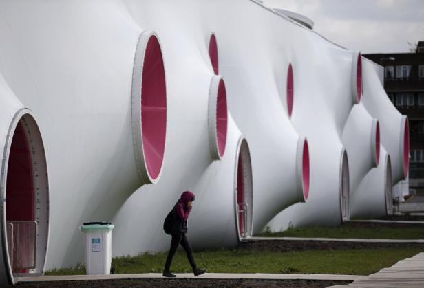 Eine Frau geht an einem ungewöhnlichen weißen Gebäude mit rosa Öffnungen vorbei.