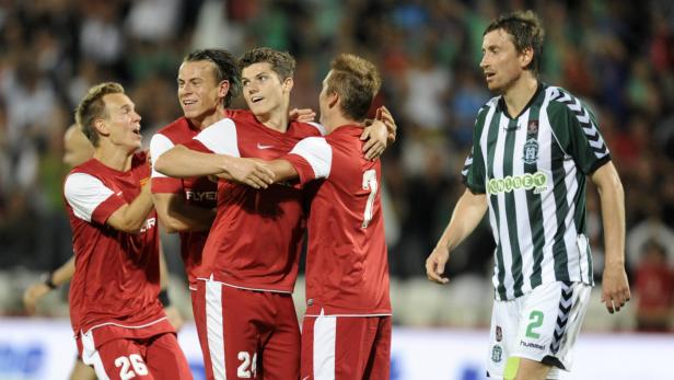 Mehrere Fußballspieler in roten Trikots umarmen sich auf dem Spielfeld.